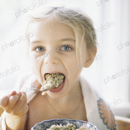 Young girl sitting at a table, eating breakfast from a bowl.
