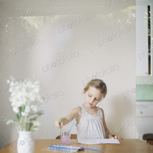 Young girl sitting at at a table, painting, a vase with white flowers. Young girl sitting at at a table, painting, a vase with white flowers.