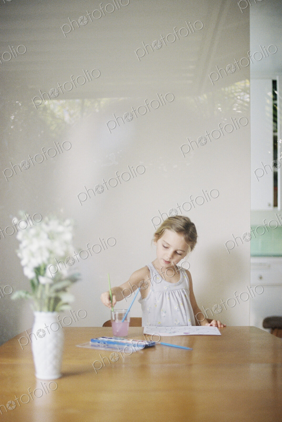 Young girl sitting at at a table, painting, a vase with white flowers.