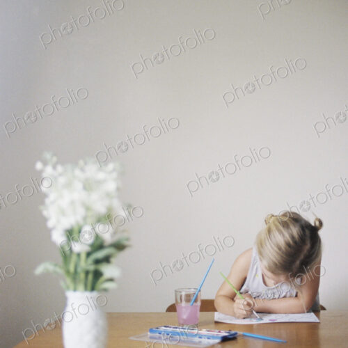 Young girl sitting at at a table, painting, a vase with white flowers. Young girl sitting at at a table, painting, a vase with white flowers.