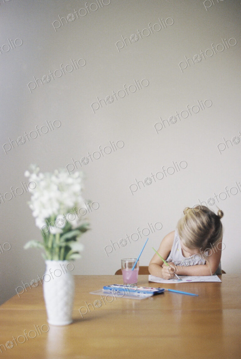 Young girl sitting at at a table, painting, a vase with white flowers.