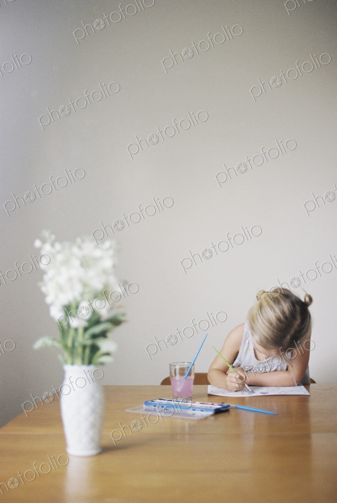 Young girl sitting at at a table, painting, a vase with white flowers.