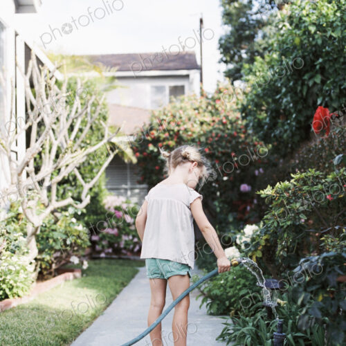 Young girl standing on a path in a garden, playing with a water hose. Young girl standing on a path in a garden, playing with a water hose.