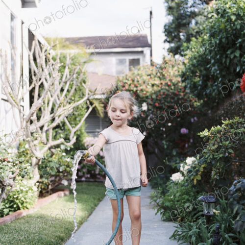 Young girl standing on a path in a garden, playing with a water hose. Young girl standing on a path in a garden, playing with a water hose.