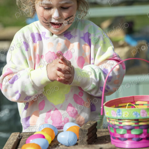 Young girl with painted face playing with Easter eggs outdoors. Young girl with painted face playing with Easter eggs outdoors.