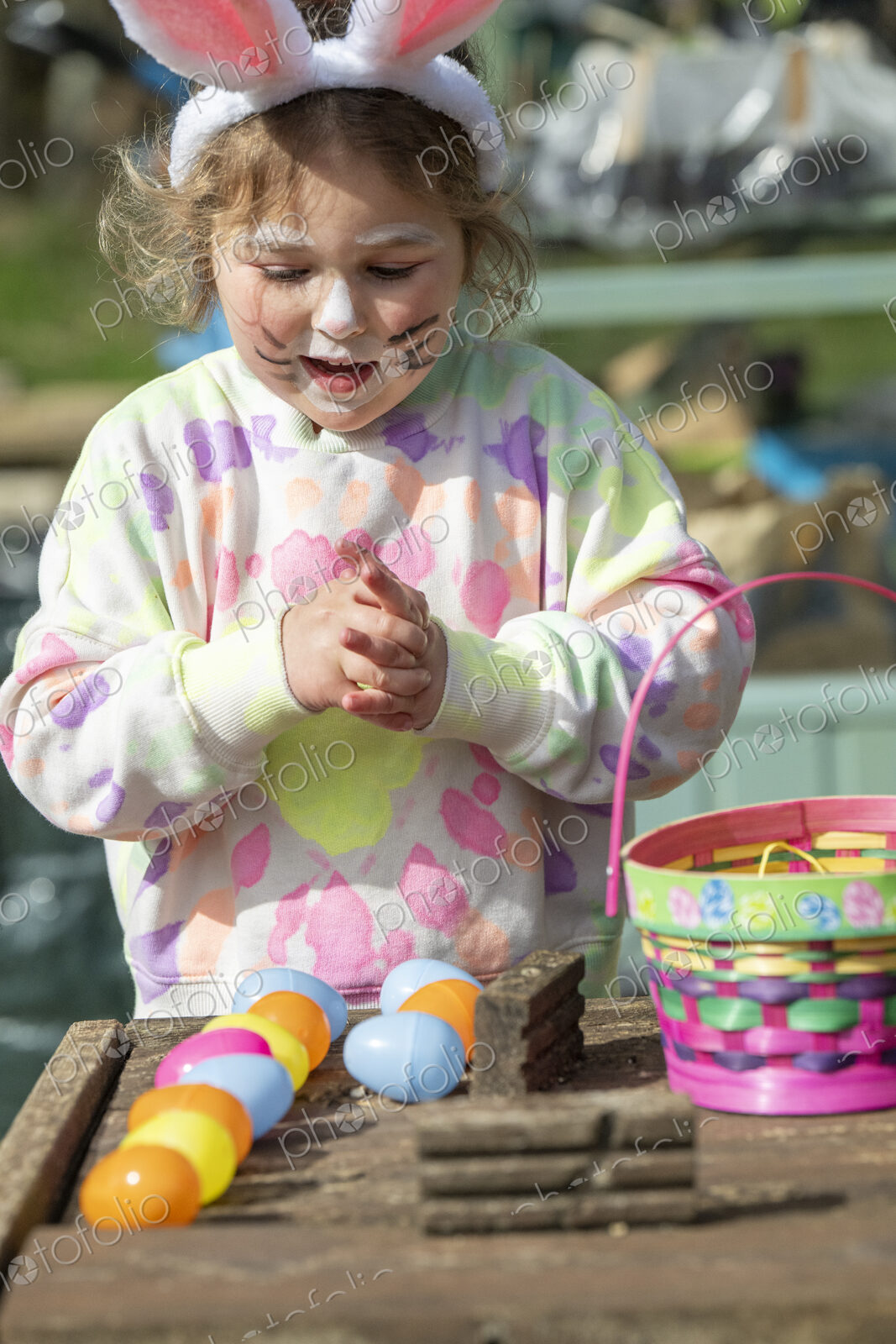 Young girl with painted face playing with Easter eggs outdoors.