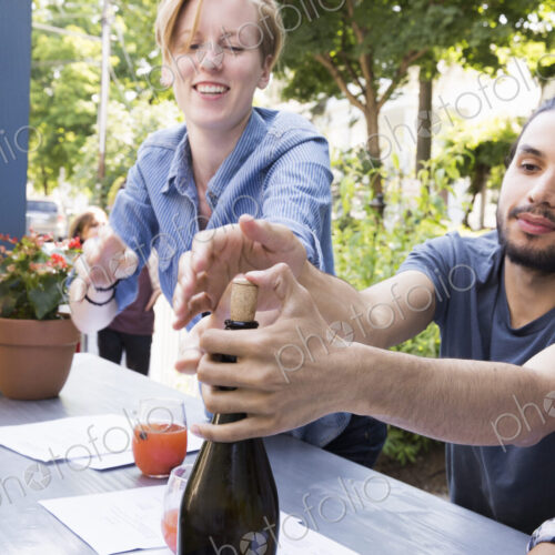 Young man and woman at a cafe, one trying to recork a bottle of wine. Young man and woman at a cafe, one trying to recork a bottle of wine.