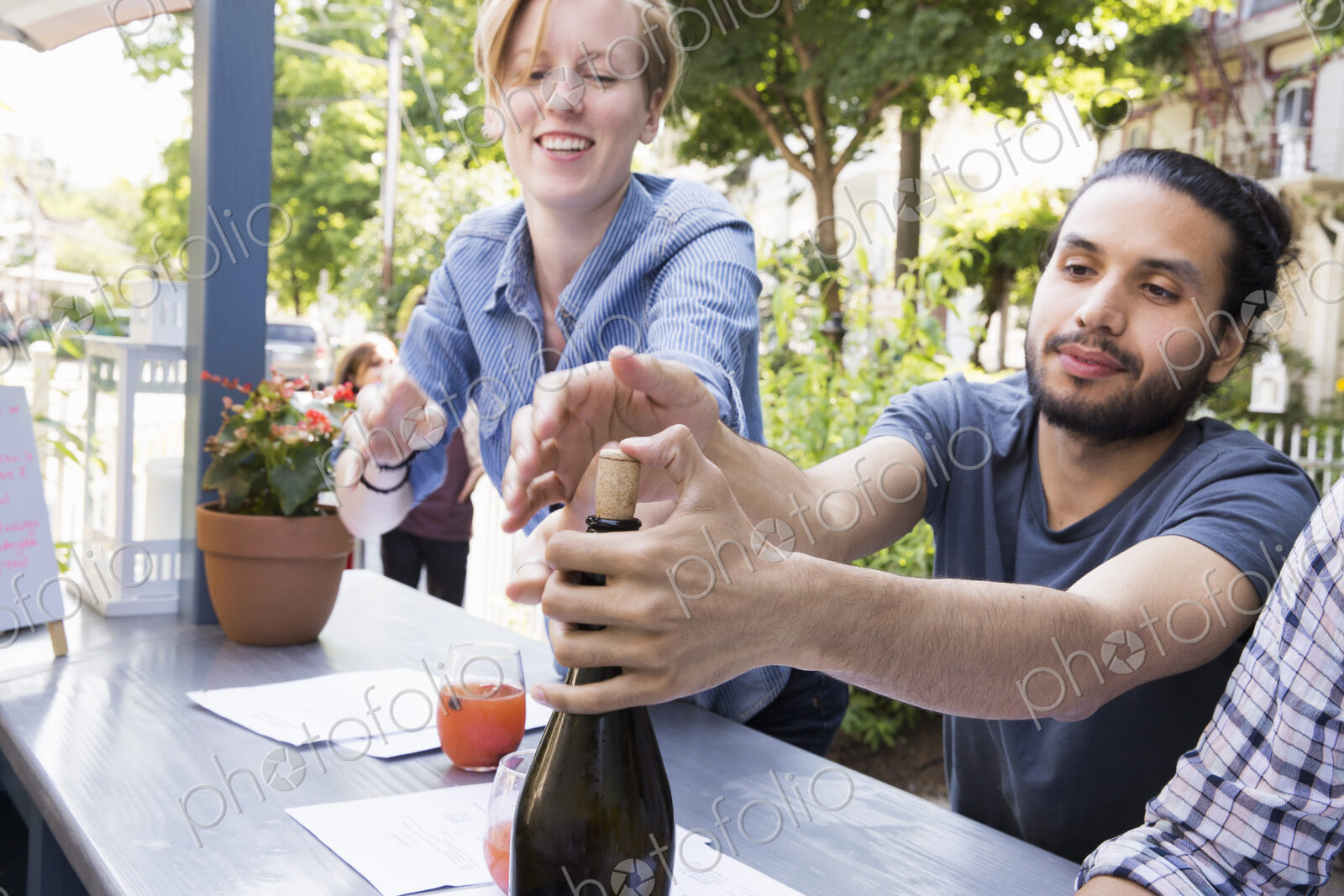 Young man and woman at a cafe, one trying to recork a bottle of wine.