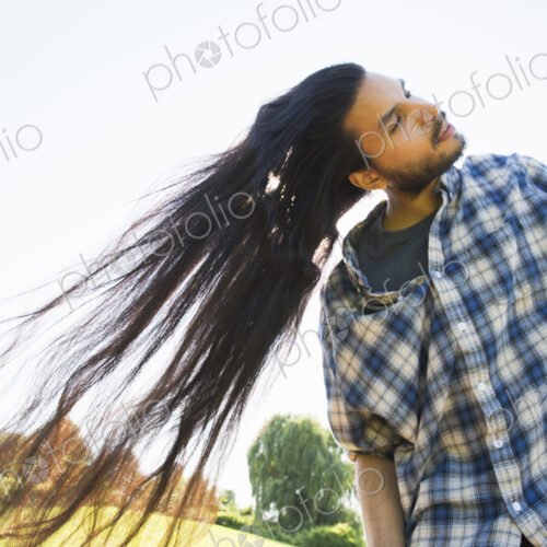 Young man shaking out his long black hair, tilting his head
