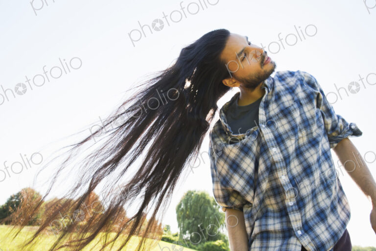 Young man shaking out his long black hair, tilting his head
