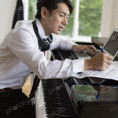 Young man sitting at a grand piano in a rehearsal studio, annotating sheet music. Young man sitting at a grand piano in a rehearsal studio, annotating sheet music.