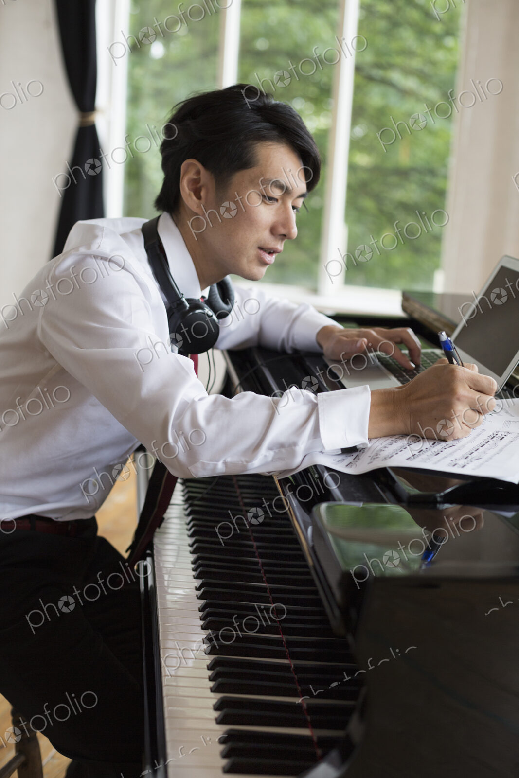Young man sitting at a grand piano in a rehearsal studio, annotating sheet music.
