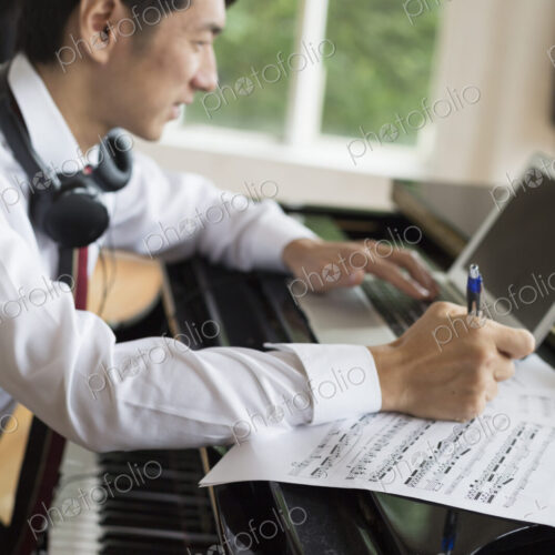 Young man sitting at a grand piano in a rehearsal studio, annotating sheet music. Young man sitting at a grand piano in a rehearsal studio, annotating sheet music.