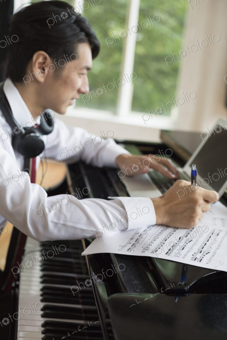 Young man sitting at a grand piano in a rehearsal studio, annotating sheet music.