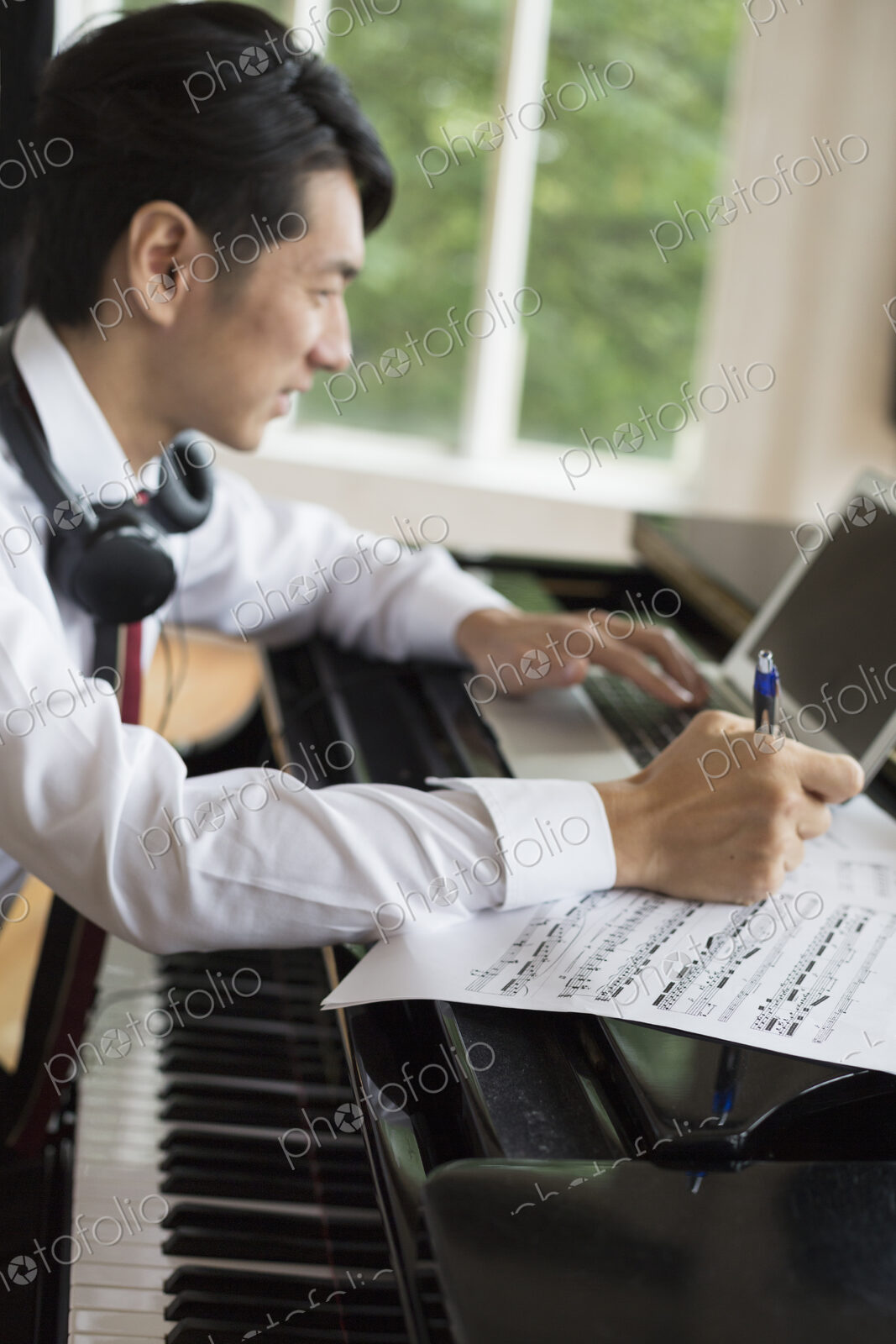 Young man sitting at a grand piano in a rehearsal studio, annotating sheet music.