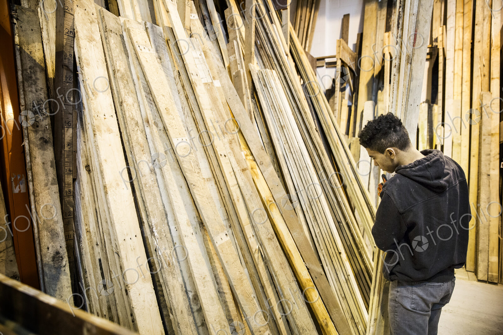 Young man standing next to a stack of wooden planks in a warehouse.