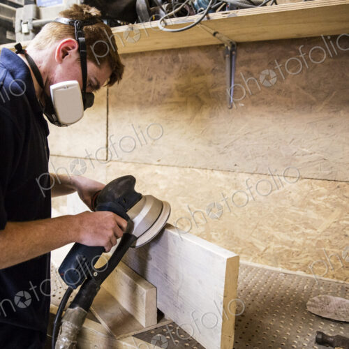 Young man wearing dust mask and protective goggles standing in a workshop, using… Young man wearing dust mask and protective goggles standing in a workshop, using…