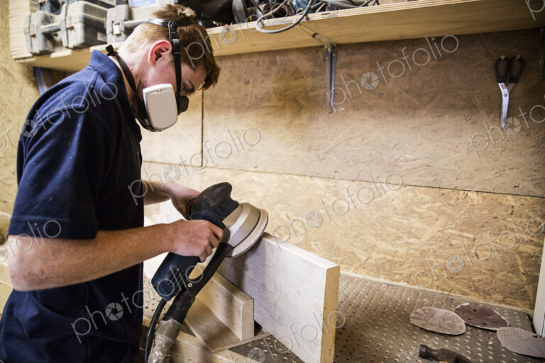 Young man wearing dust mask and protective goggles standing in a workshop, using…