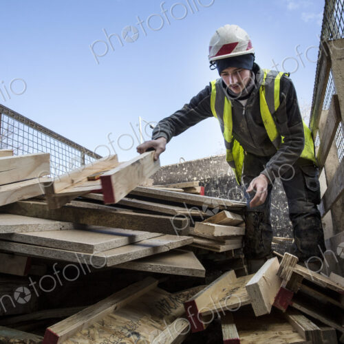 Young man wearing hard hat and reflective vest standing on top of stack of recycled wood. Young man wearing hard hat and reflective vest standing on top of stack of recycled wood.