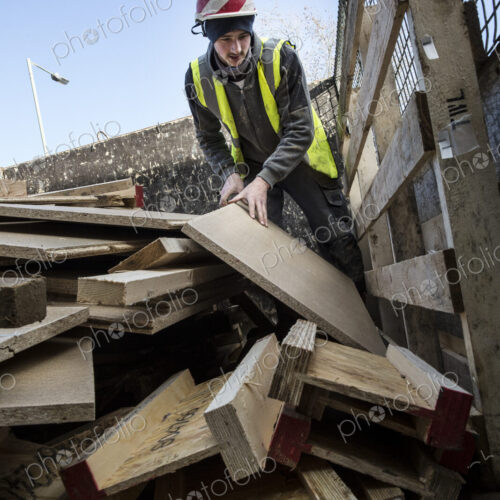 Young man wearing hard hat and reflective vest standing on top of stack of recycled wood. Young man wearing hard hat and reflective vest standing on top of stack of recycled wood.