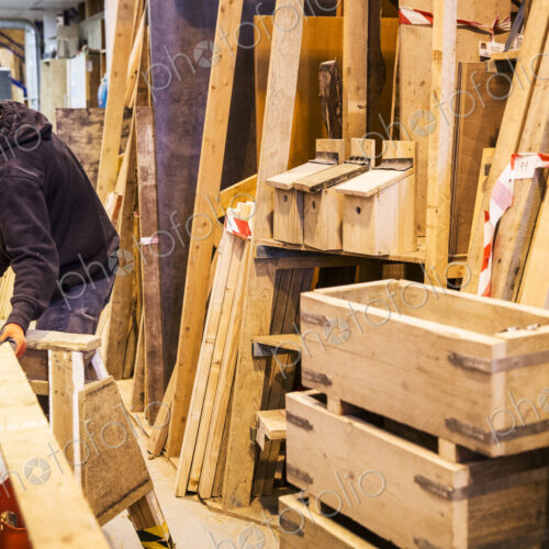Young man wearing work gloves standing in warehouse, balancing plank of wooden on… Young man wearing work gloves standing in warehouse, balancing plank of wooden on…