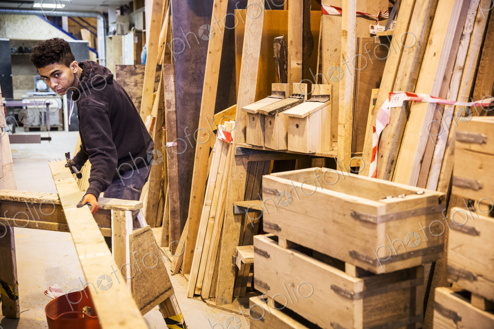 Young man wearing work gloves standing in warehouse, balancing plank of wooden on…