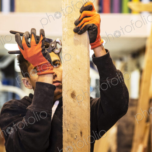 Young man wearing work gloves standing in warehouse, removing rusty nails from… Young man wearing work gloves standing in warehouse, removing rusty nails from…