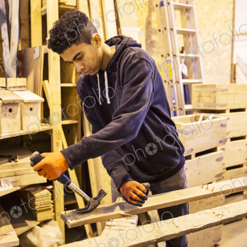 Young man wearing work gloves standing in warehouse, removing rusty nails from… Young man wearing work gloves standing in warehouse, removing rusty nails from…