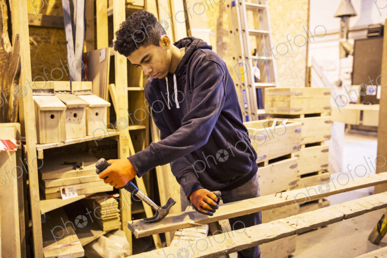Young man wearing work gloves standing in warehouse, removing rusty nails from…