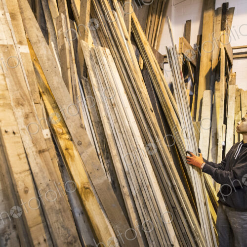 Young man wearing work gloves standing next to a stack of wooden planks in a warehouse. Young man wearing work gloves standing next to a stack of wooden planks in a warehouse.