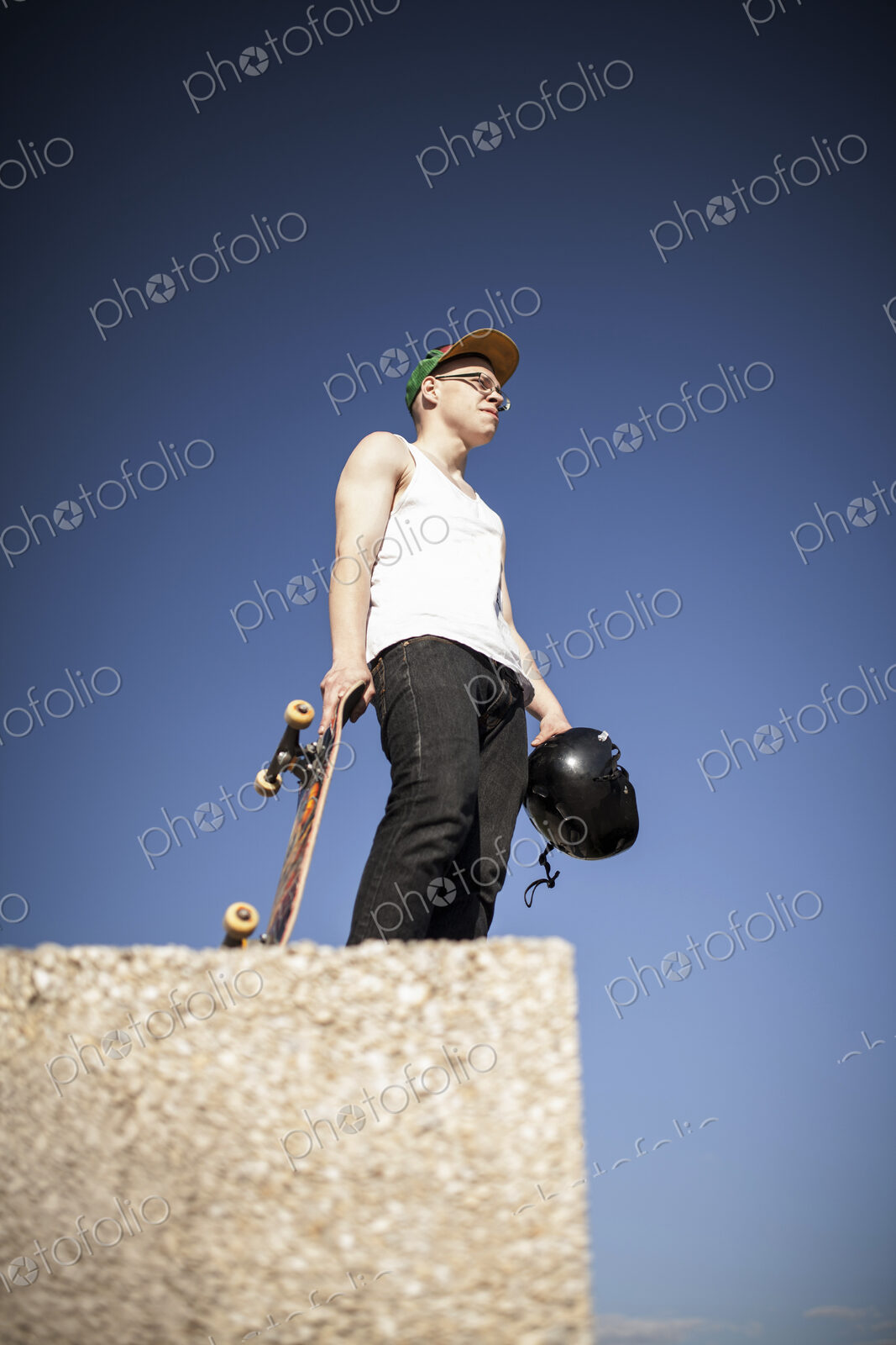 Young man with skateboard standing on top of half pipe in skate park.