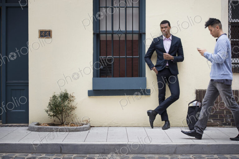 Young people outdoors on the city streets in springtime. A man leaning against a wall…