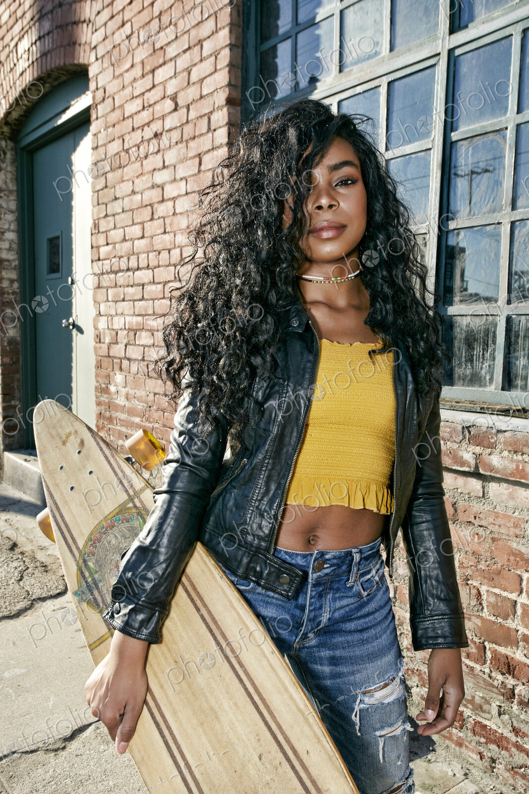 Young smiling woman with long curly black hair standing on pavement, holding…