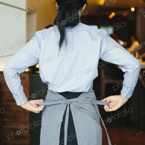 Young waitress tying her apron at a city restaurant. Young waitress tying her apron at a city restaurant.