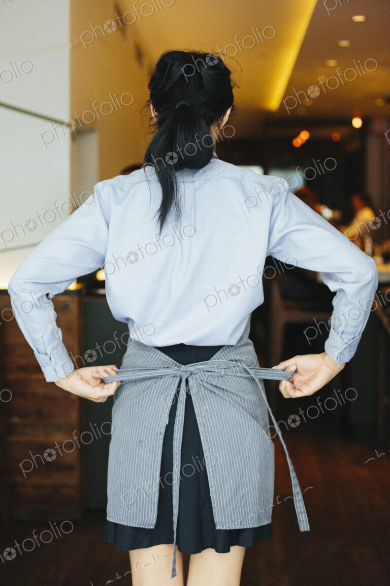 Young waitress tying her apron at a city restaurant.