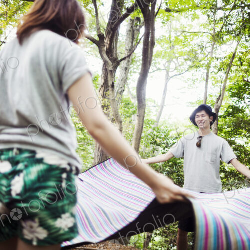 Young woman and man standing in a forest, holding a picnic rug. Young woman and man standing in a forest, holding a picnic rug.