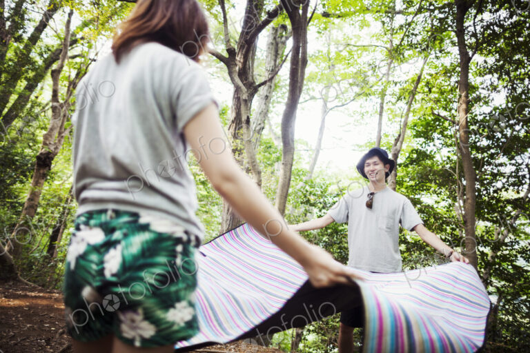Young woman and man standing in a forest, holding a picnic rug.
