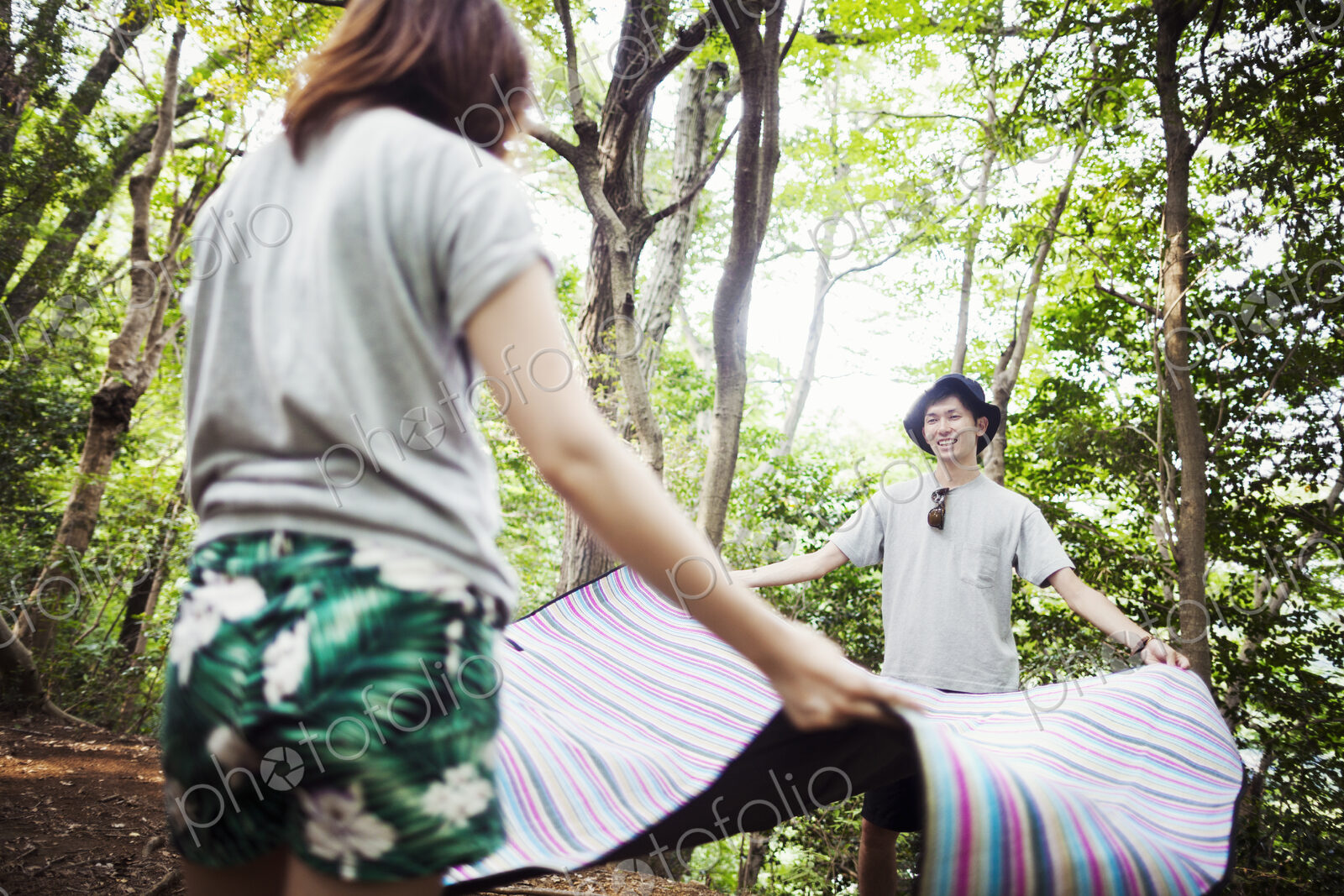 Young woman and man standing in a forest, holding a picnic rug.