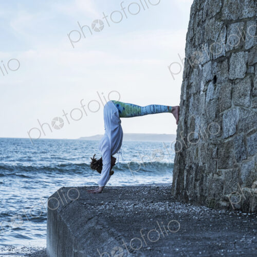 Young woman doing handstand by the ocean, with her legs against a wall. Young woman doing handstand by the ocean, with her legs against a wall.