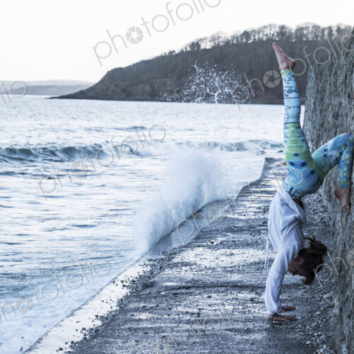 Young woman doing handstand on a wall by the ocean, one leg raised. Young woman doing handstand on a wall by the ocean, one leg raised.