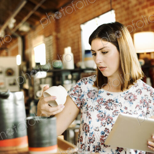 Young woman in a shop, holding a digital tablet and a ceramic mug. Young woman in a shop, holding a digital tablet and a ceramic mug.