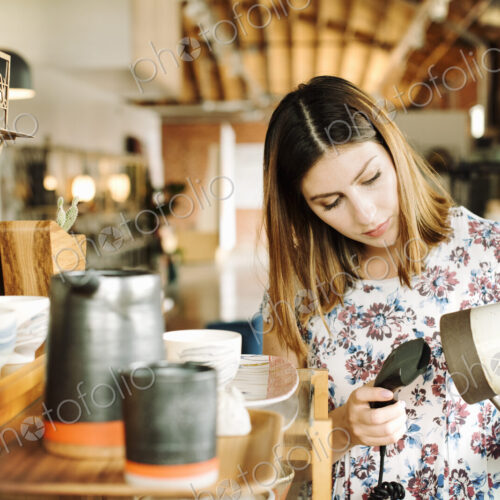 Young woman in a shop, scanning the barcode of a ceramic jug with a barcode scanner. Young woman in a shop, scanning the barcode of a ceramic jug with a barcode scanner.