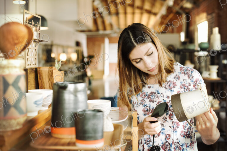 Young woman in a shop, scanning the barcode of a ceramic jug with a barcode scanner.