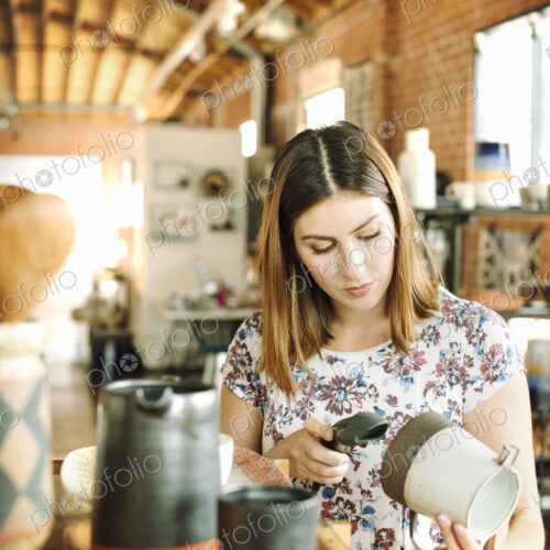 Young woman in a shop, scanning the barcode of a ceramic jug with a barcode scanner. Young woman in a shop, scanning the barcode of a ceramic jug with a barcode scanner.