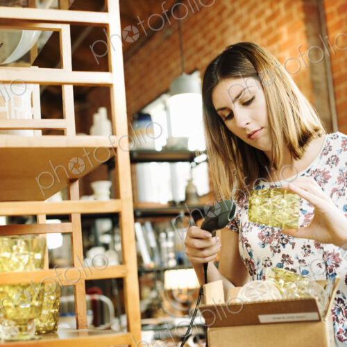 Young woman in a shop, scanning the barcode of a drinking glass with a barcode scanner. Young woman in a shop, scanning the barcode of a drinking glass with a barcode scanner.