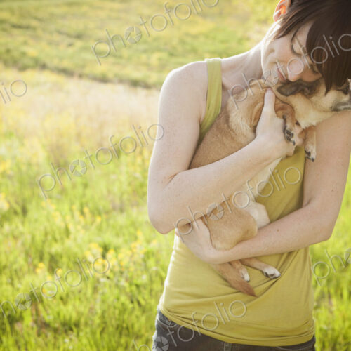 Young woman in grassy field in spring holding dog Young woman in grassy field in spring holding dog