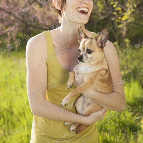 Young woman in grassy field in spring holding dog Young woman in grassy field in spring holding dog