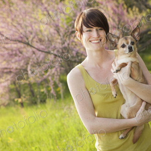 Young woman in grassy field in spring holding dog Young woman in grassy field in spring holding dog