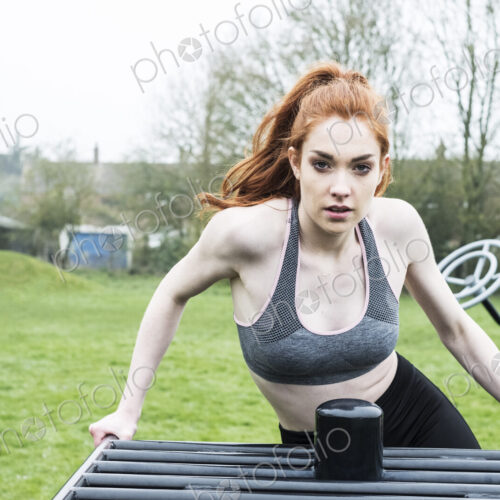 Young woman in sportswear using outdoor exercise equipment