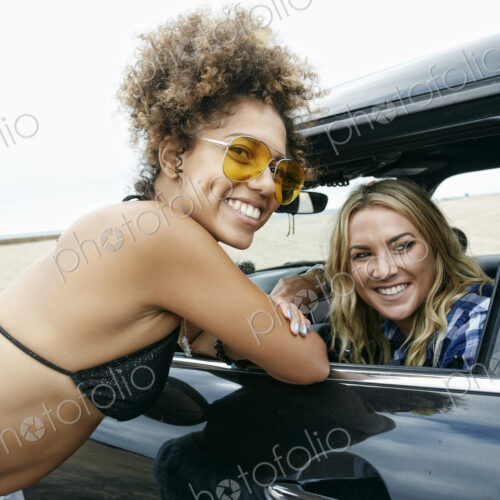 Young woman leaning against car door talking to a woman driver, friends
